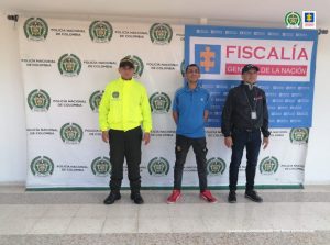 en la imagen se ve una persona detenida bajo custodia de un servidor del CTI y la Policía. Detrás suyo backings de cada una de las instituciones.