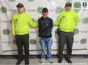 En la fotografía aparece un capturado, junto a personal de Policía Nacional y Fiscalía General de La Nación. En la parte posterior de la imagen se ven banners de Policía Nacional y la Fiscalía General de la Nación.  