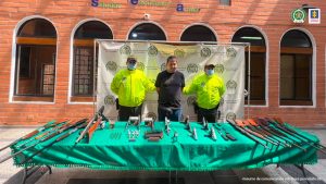 En la fotografía está el procesado con 2 servidores de la Policía Nacional y una mesa con todas las armas y municiones incautadas