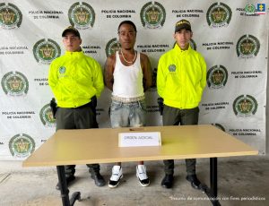 En la fotografía está el capturado junto a dos agentes de la Policía Nacional. En la parte superior está un banner de la Policía Nacional