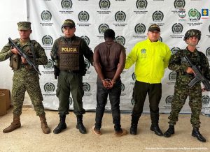 En la foto aparece el capturado junto a dos agentes a la Policía Nacional y dos infantes de la Armada Nacional. En la parte superior está un banner de la Policía Nacional