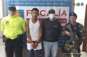 En la fotografía aparece una persona capturada, acompañada de un servidor del (CTI) y dos uniformados de La Policía y el Ejército Nacional. En la parte posterior un banner con logos de la Fiscalía. 