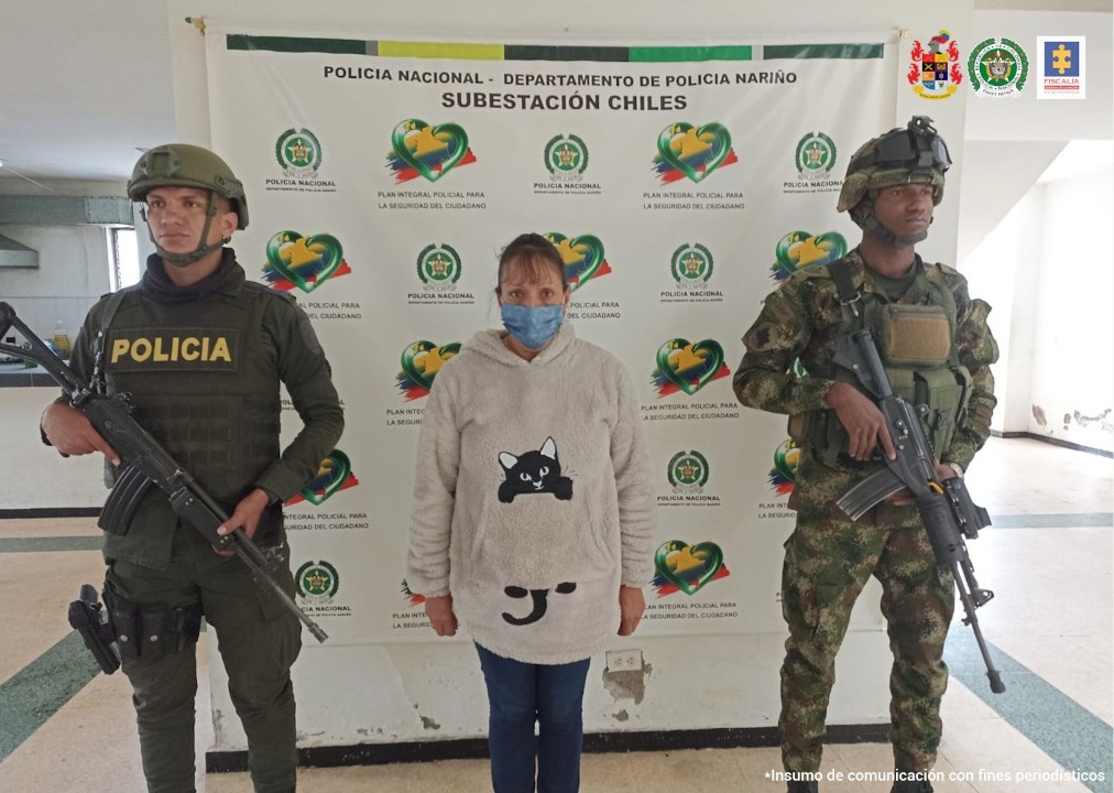En fotografía aparece una mujer con tapabocas capturada, junto a personal de la Policía y el Ejército. En la parte posterior de la imagen se ve un banners de la Policía Nacional