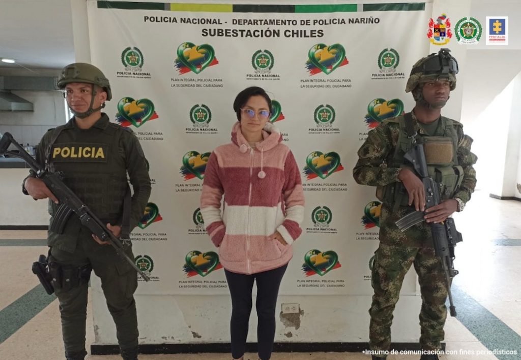 En fotografía aparece una mujer con tapabocas capturada, junto a personal de la Policía y el Ejército. En la parte posterior de la imagen se ve un banners de la Policía Nacional
