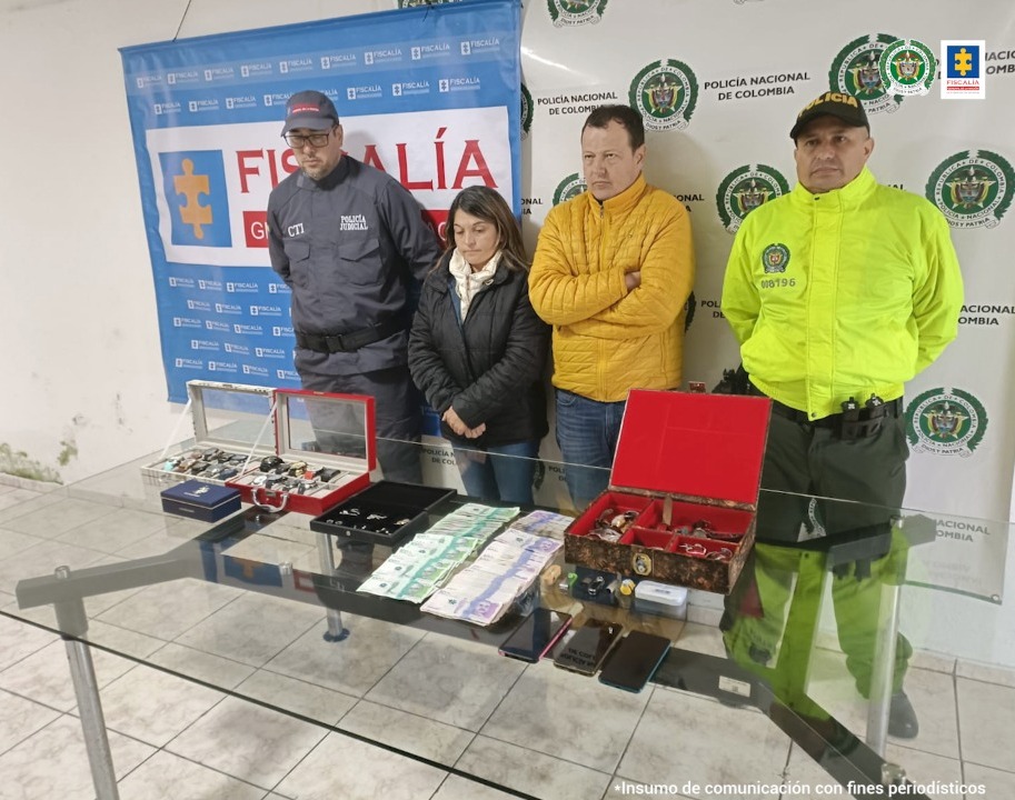 En la foto están los detenidos detrás de una mesa donde se observan las joyas incautadas. Están acompañados de funcionarios del CTI y de la Policía Nacional. Atrás se observan baners de la Fiscalía y la Policía.