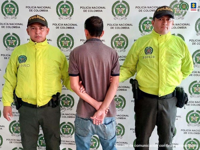 En la fotografía aparece el capturado de espaldas, junto a dos uniformados de la Policía Nacional. En la parte posterior se visualiza banner de la Policía Nacional