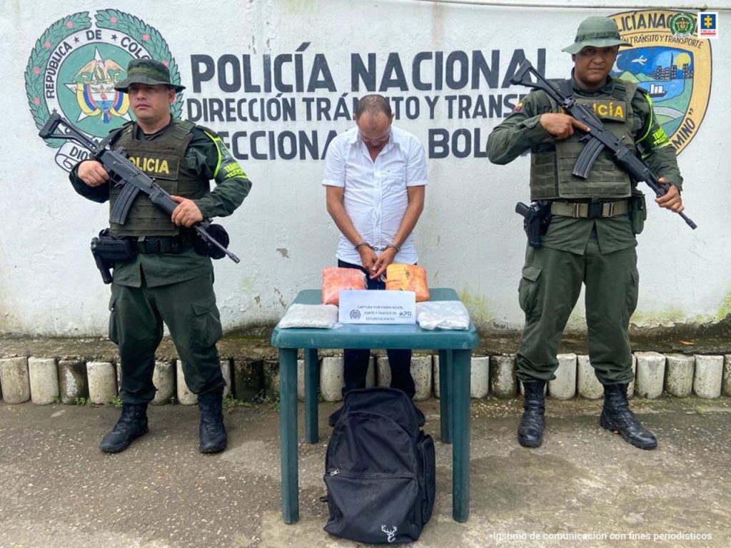 En la fotografía aparece el capturado con una camisa blanca y el rostro agachado acompañado de dos uniformados de la Policía Nacional delante de un pendón de esa institución. También se observa una mesa con mantel blanco y el estupefaciente que se incautó.