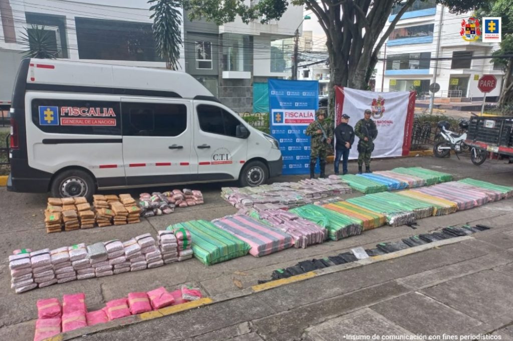 En la fotografía aparecen varios bultos de colores que contienen marihuana junto a dos soldados del Ejército Nacional. En la parte posterior aparece un banner de la Fiscalía General de la Nación y otro del Ejército Nacional.