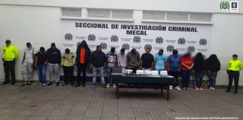 En la fotografía aparecen 15 personas capturadas, tres mujeres y 12 hombres, una de las cuales fue dejada en libertad, junto a dos agentes de la Policía Metropolitana. En frente de los detenidos hay una mesa en la que se observa el material incautado por las autoridades.