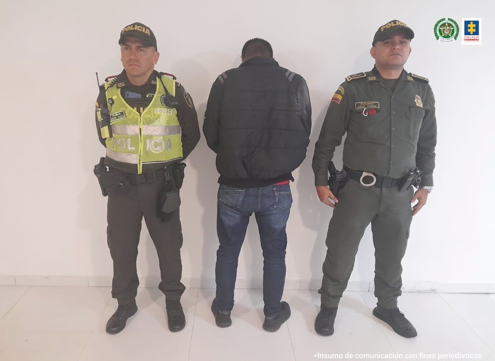 En la foto se ve un hombre de espaldas con chaqueta y jean custodiado por dos uniformados de la Policía Nacional.