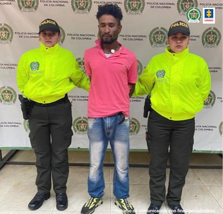 En la fotografía aparece un capturado, junto a personal de Policía Nacional. En la parte posterior de la imagen se ven banners de Policía Nacional y la Fiscalía General de la Nación.