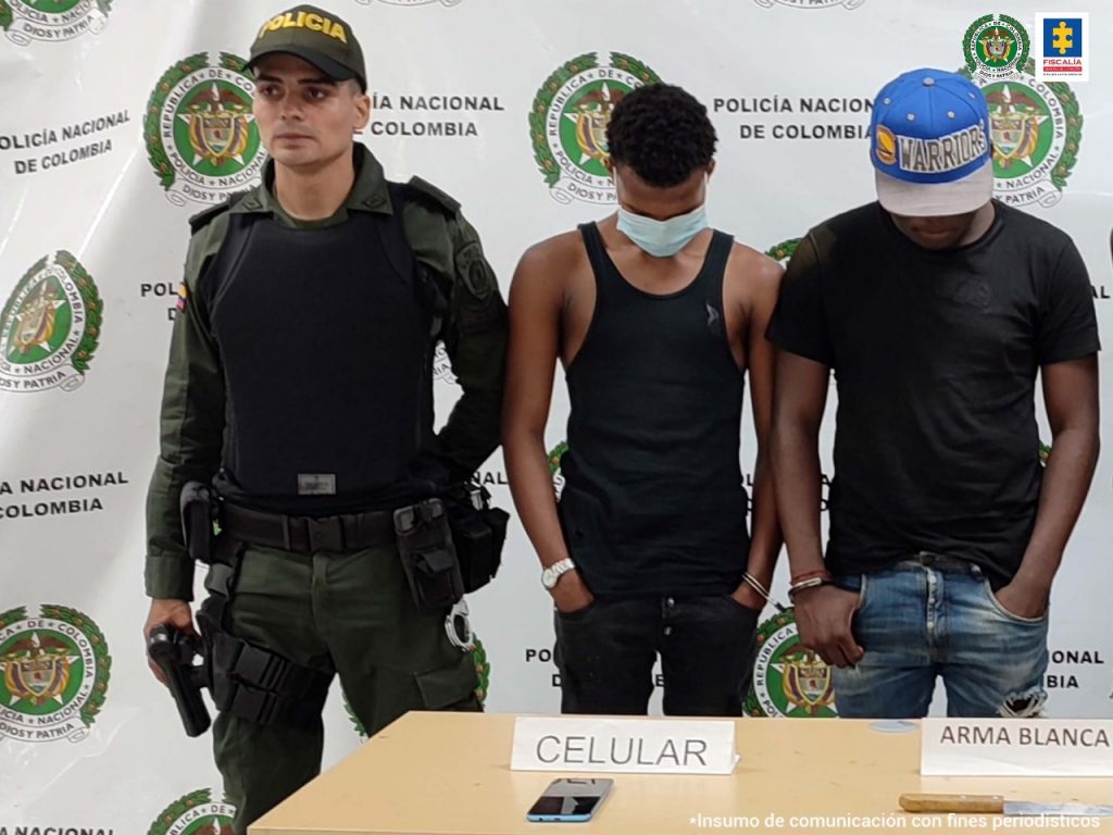 En la fotografía aparecen dos personas capturadas junto a un agente de la Policía. En la parte posterior, se ve un banner de la Policía Nacional