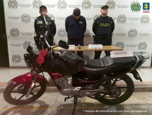Fiscal Mancera, Fiscal Martha Mancera, Martha Mancera, Fiscalía General de la Nación Se observa el capturado en el centro y un uniformado de Policía Nacional a cada costado. Al fondo un pendón de Policía Nacional. Adelante una mesa con objetos recuperados y la moto presumiblemente utilizada en el ilícito