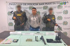 Fiscal Mancera, Fiscal Martha Mancera, Martha Mancera, Fiscalía General de la Nación En la fotografía se encuentra un hombre trigueño, de pie, con los brazos atrás, vestido de buzo gris y jean azul custodiado por dos agentes de la Policía Nacional. Delante de ellos hay una mesa con el arma y las municiones que se le incautaron.