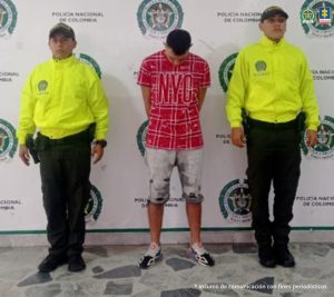 Fiscal Mancera, Fiscal Martha Mancera, Martha Mancera, Fiscalía General de la Nación en la imagen se ve una persona detenida bajo custodia de dos integrantes de la Policía Nacional. Detrás suyo un backing institucional.