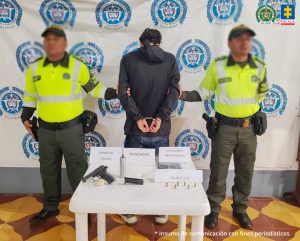 Fiscal Mancera, Fiscal Martha Mancera, Martha Mancera, Fiscalía General de la Nación En las tres fotografías se observa al capturado en el centro y a cada costado un uniformado de la Policía Nacional. Atrás un pendón de Policía Nacional y delante una mesa en la cual está expuesto el material incautado.
