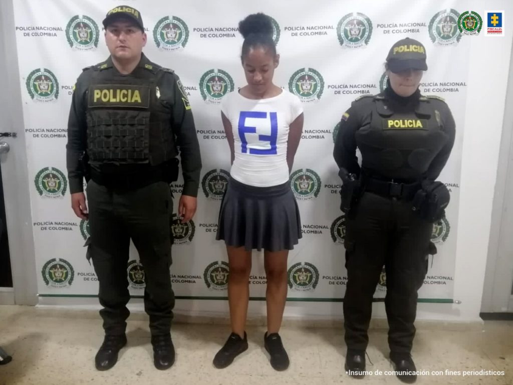 En la fotografía aparece una mujer capturada junto a dos agentes de la Policía Nacional. En la parte posterior se ve un banner de la Policía Nacional 