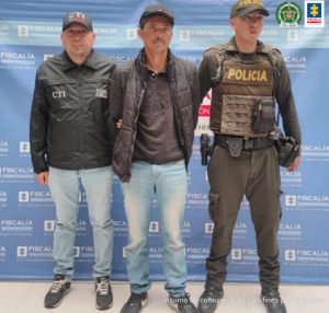 En la fotografía aparece el capturado junto a un servidor del CTI y un agente de la Policía Nacional. En la parte superior está un banner de la Fiscalía General de la Nación