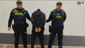 El capturado está en medio de dos uniformados de la policía nacional, está vestido de negro.