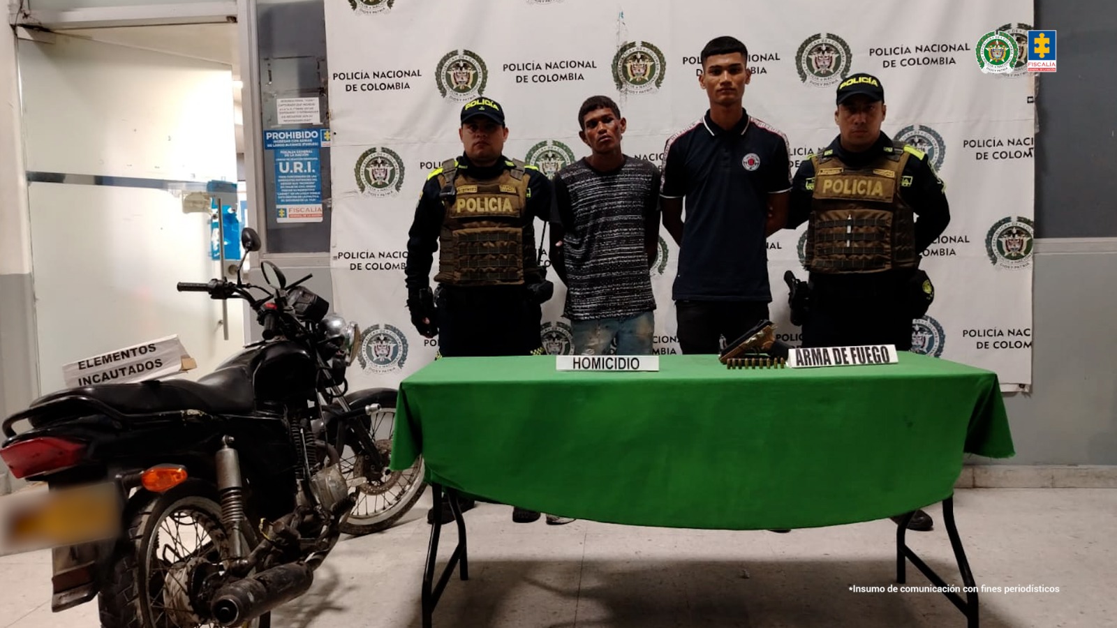 En la fotografía se observan cuatro personas, dos de ellas los procesados y dos uniformados de la Policía Nacional. En la parte posterior un backing con escudos de la Policía.