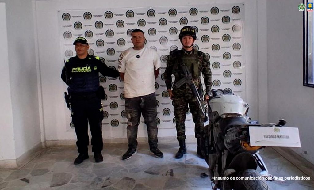 En la foto aparece el capturado de frente y custodiado por uniformados de la Policía Nacional. En la foto también aparece la moto que incautaron. 