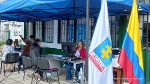 En la imagen se ve una carpa azul, donde están dos servidores de la entidad atendiendo a los usuarios. Así mismo se ve la bandera de la Fiscalía y la de la República de Colombia.