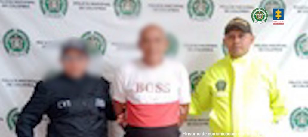 En la imagen aparece una persona con suéter de dos colores, entre uniformados del CTI y de la Policía.