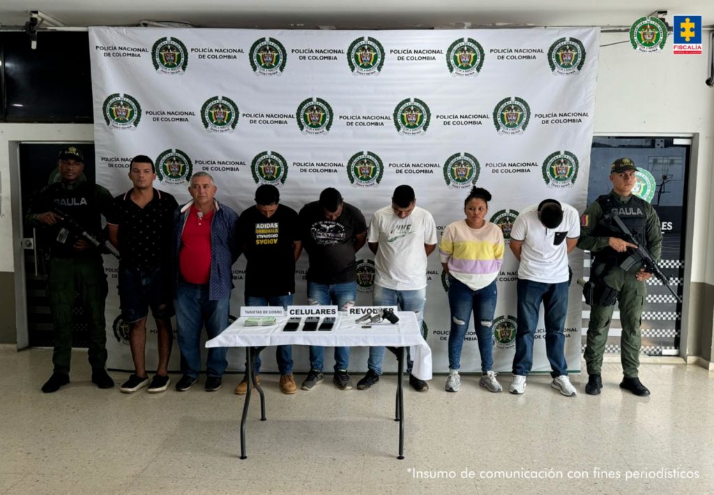 En la imagen aparecen siete personas detenidas entre uniformados de la Policía Nacional frente a una mesa con un revólver y varios celulares.