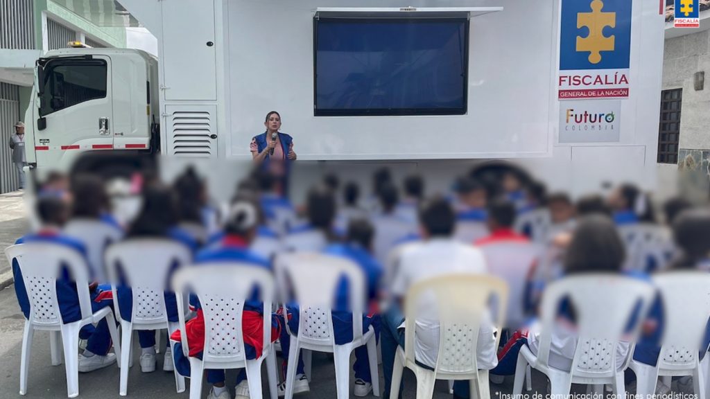 En las dos fotografías se aprecia a grupos grandes de estudiantes, una de ellas al aire, sentados en sillas blancas. Una servidora del programa ‘Futuro Colombia’ comparte con los estudiantes una proyección en una pantalla que tiene como fondo un vehículo denominado como Unidad Móvil de la Fiscalía.