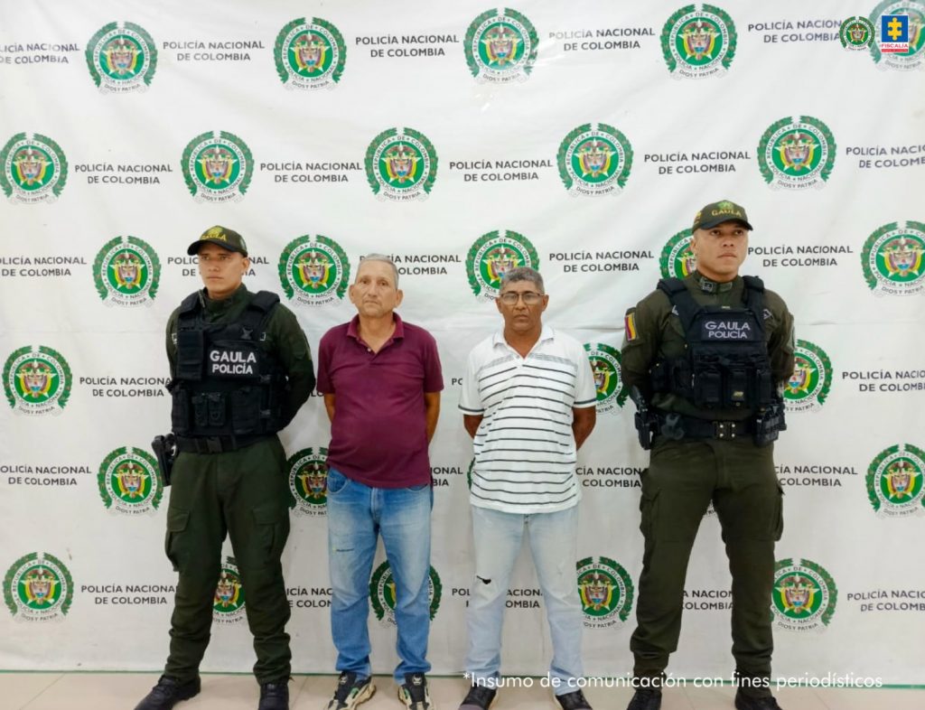 En la imagen aparecen dos personas, una de ellas con gafas, entre dos uniformados de la Policía Nacional.