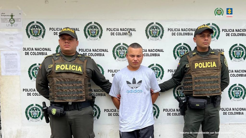 En la imagen aparece una persona de suéter gris entre dos uniformados de la Policía.