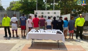 En la fotografía se encuentran diez capturados de pie, de espalda, esposados, custodiado por dos uniformados de la Policía Nacional. Delante de ellos hay una mesa con las armas, municiones y la droga incautada.