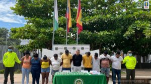 En la fotografía se observan a los capturados custodiados por dos agentes de la Policía Nacional y detrás de ellos un pendón de esa institución. Igualmente se visibiliza una mesa con mantel verde donde se muestra la droga y los celulares incautados.