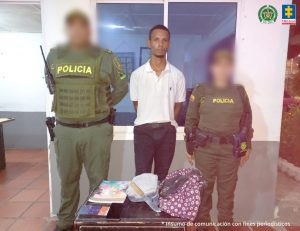 En la fotografía aparece un hombre de pie, con los brazos atrás, delgado, trigueño, vestido con camisa blanca manga corta y pantalón oscuro, custodiado por dos agentes de la Policía Nacional. Delante de ellos hay una mesa donde están un cuchillo, el bolso y el celular que presuntamente hurtó.