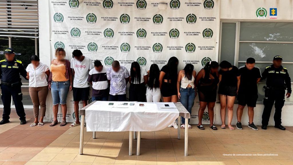 En la fotografía están los procesados de pie, de frente, con los brazos esposados, custodiados por uniformados de la Policía Nacional. Detrás de ellos hay un pendón de esa institución.
