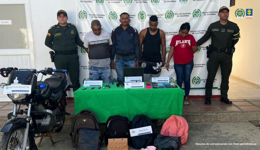 En la fotografía están tres hombres y una mujer de pie, de frente, con las muñecas esposadas entre ellos, custodiado por dos uniformados de la Policía Nacional. Delante de ellos hay una mesa con celulares, el arma de fuego, las armas blancas y con los elementos que habían hurtado.