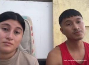 En la fotografía aparecen una mujer y un hombre ambos de cabellos lisos negros, trigueños, ella vestida con camiseta beige y el con camisilla roja. Ambos están sentados asistiendo virtualmente a la audiencia en la que se les procesó. 