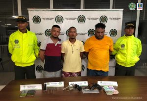 En la fotografía se observan a tres hombres custodiado por dos agentes de la Policia Nacional, con las armas y el dinero que les fueron incautados en los operativos.