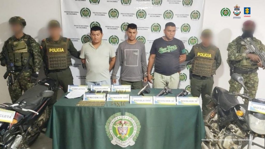 En la foto están tres hombres de pie, trigueños, con los brazos atrás esposados, vestidos con camisetas, custodiados por uniformados de la Policía Nacional. 