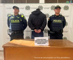  En la fotografía está un hombre de pie, de espalda, con los brazos esposados, vestido con una chaqueta negra, jean azul y se encuentra custodiado por dos uniformados de la Policía Nacional. 