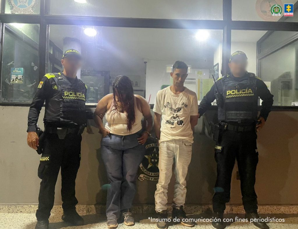 En la fotografía aparece una mujer de contextura gruesa y pelo largo, a su lado está un hombre delgado, ambos de pie, de frente, con los brazos atrás esposados en las afueras de un CAI y están custodiados por dos uniformados de la Policía Nacional.