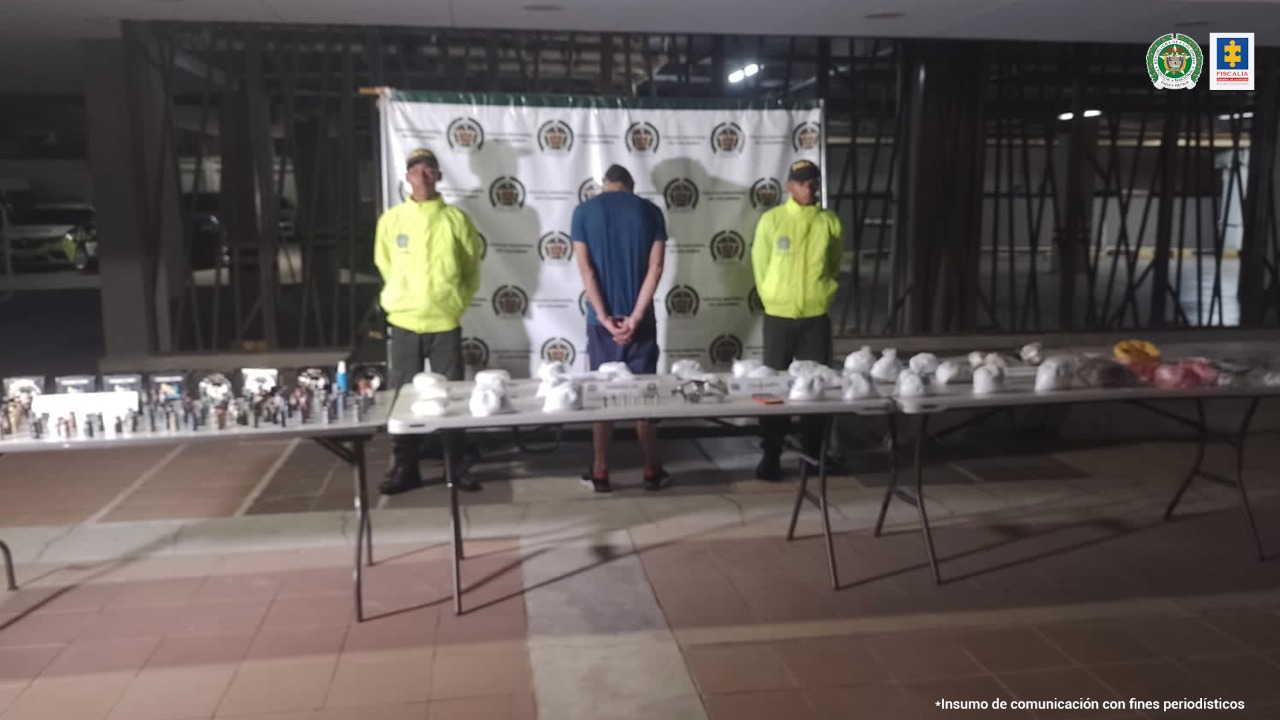 En la imagen aparece un hombre de espalda custodiado por dos uniformados de la Policía Nacional delante de un pendón de esa institución. Delante del capturado se observa una mesa con unas bolsas llenas de estupefacientes.