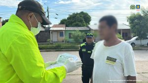 En las fotografía, aparece un hombre moreno, de estatura media, cabellos negros cortos, vestido con camiseta blanca y pantalón azul, tiene el rostro difuminado y está custodiado por dos uniformados de la Policía Nacional.  
