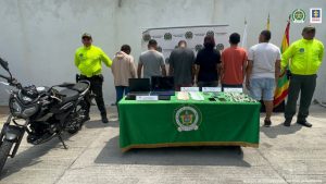 En la imagen se observa a los procesados de espalda delante custodiados por dos agentes de la Policía Nacional, delante de un pendón de esa institución.