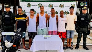 En la fotografía aparecen los seis procesados de frente, de pie, con los brazos atrás esposados, custodiados por dos uniformados de la Policía Nacional.