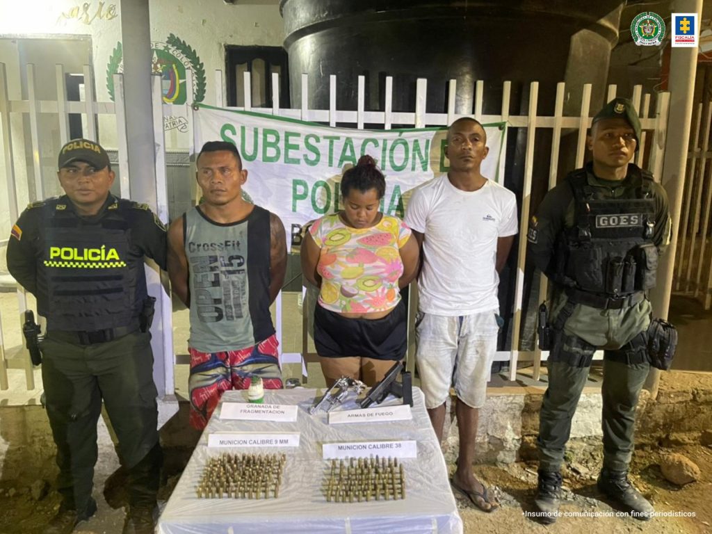 En la fotografía se observan a dos hombres y una mujer, custodiados por dos agentes de la Policía Nacional, delante de una mesa blanca donde se destaca la munición, el arma y la pistola incautada.
