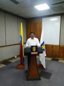En la fotografía se observa a un funcionario de la Fiscalía leyendo el acta de entrega oficial de los restos de una víctima detrás de un atril, acompañado por las banderas de la Fiscalía General y de Colombia.