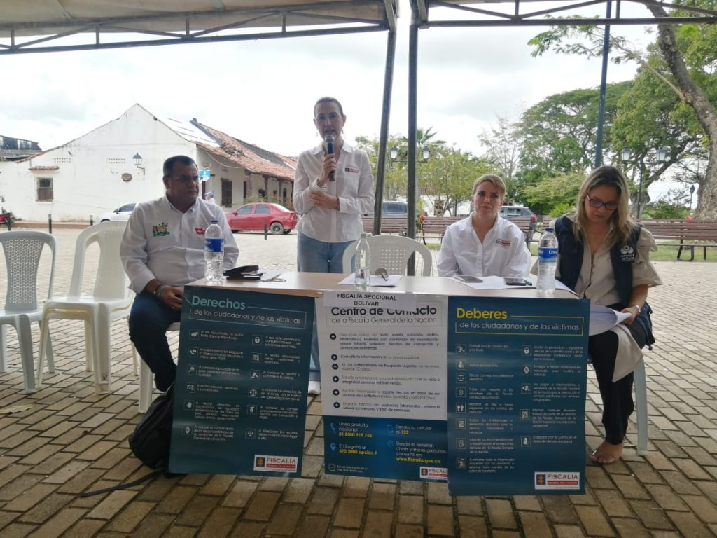 En la imagen aparece sentados dos mujeres y un hombre. De pie se encuentra otra mujer con un micrófono instalando el evento.