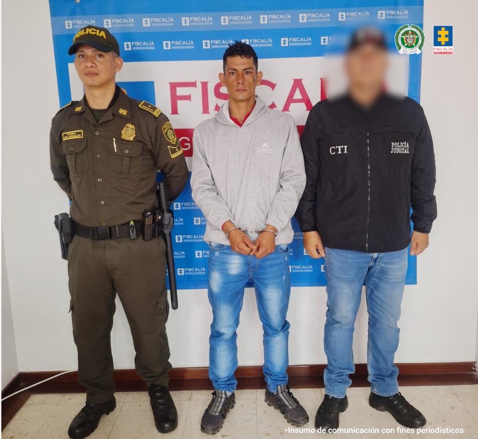 En la fotografía se aprecia de pie, con los brazos adelante y esposado a Daniel Grajales Bedoya. Viste buso gris de manga larga, jean azul desgastado y zapatillas negras con gris. Al lado izquierdo de él hay un servidor del CTI de la Fiscalía y al derecho un uniformado de la Policía Nacional. Detrás de ellos hay un pendón institucional de la Fiscalía.
