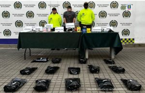 En la foto aparece de pie y de espaldas a la cámara, Jefferson Arbey Ospina Navia. Viste camiseta de manga corta con estampado tipo camuflado. A lado y lado de él hay dos uniformados de la Policía Nacional. Delante de ellos hay una mesa con mantel verde y sobre ella hay varios letreros que dicen: ‘Cocaína’, ‘WAX’, ‘Droga sintética’, ‘Pastillas’, ‘Marihuana’, ‘Munición’ y ‘Arma de fuego’. Asimismo se aprecian elementos alusivos a dicha información. Igualmente, en el suelo hay 14 bolsas negras. En la parte posterior hay un pendón institucional de la Policía.